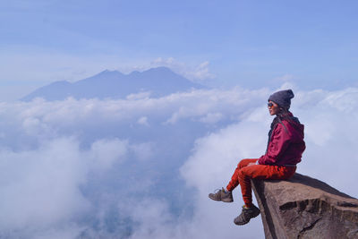 Side view of woman sitting on rock against sky