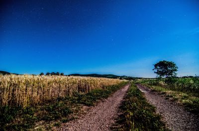 Road passing through field against cloudy sky