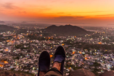 Low section of man looking at cityscape during sunset