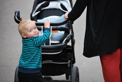 Portrait of boy pushing baby stroller with mother on footpath at park