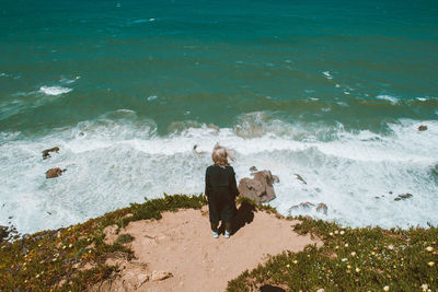 Rear view of woman standing on cliff by sea