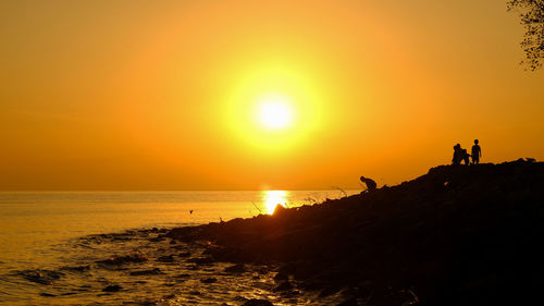 Silhouette people on beach against sky during sunset