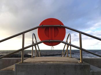 Life belt on railing by sea against cloudy sky