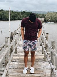 Rear view of man standing on railing against water