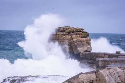 Waves splashing on rocks at shore against sky