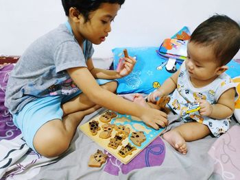 Siblings playing with toys on bed at home