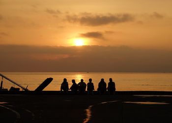 Silhouette people on sea against sky during sunset