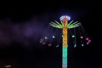 Low angle view of illuminated chain swing ride against sky at night