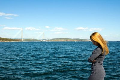 Side view of young woman standing in sea against sky