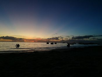 Silhouette people on beach against sky during sunset