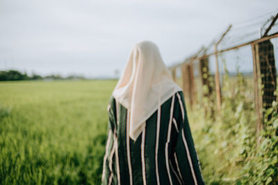 Rear view of woman standing on field against sky