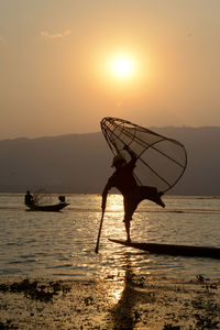 Silhouette men fishing in lake during sunset