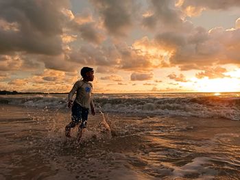 Full length of man on beach against sky during sunset