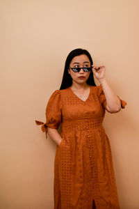 Portrait of young woman standing against nude color wall