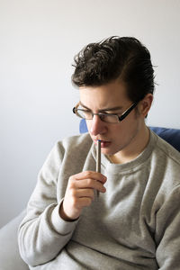 Portrait of young man holding eyeglasses against wall