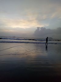 Man walking at beach against sky during sunset