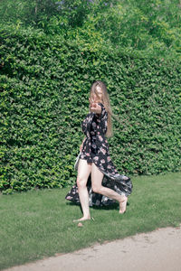 Full length portrait of woman walking on grass against plants