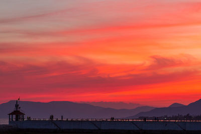 Pier at beach by mountains against orange sky