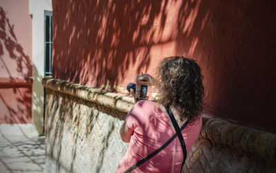 Rear view of woman photographing while standing by wall