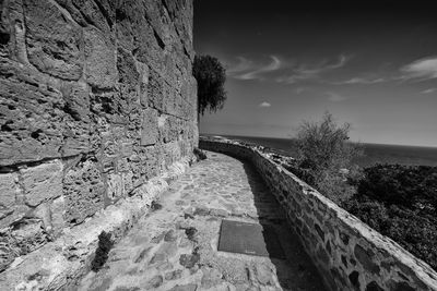 Footpath by wall against sky