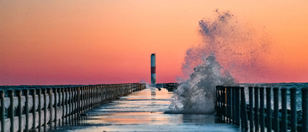 Pier over sea against orange sky