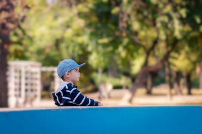 Boy looking away while standing against retaining wall in park