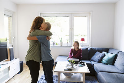 Smiling mother embracing son while daughter using digital tablet at home