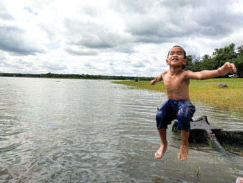 Full length of shirtless boy in lake against sky