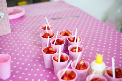 High angle view of strawberries in disposable cups on pink table