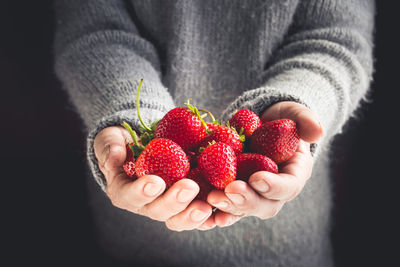 Midsection of person holding strawberries against black background