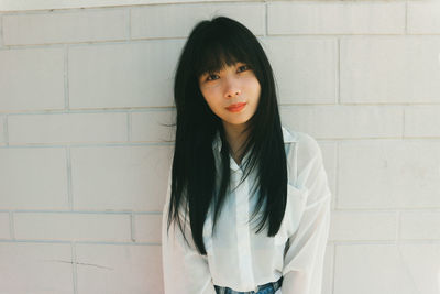 Portrait of a beautiful young woman standing against wall