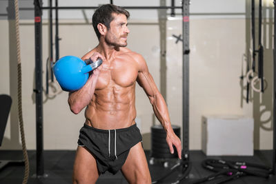 Shirtless man exercising with kettlebell in gym