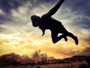 Low angle view of silhouette man jumping against sky at sunset