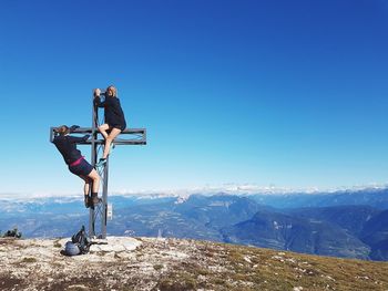 Women climbing on cross over mountain against clear blue sky
