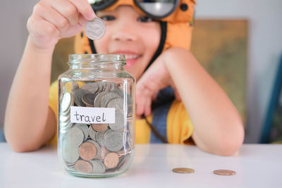 Midsection of woman putting coin in jar on table