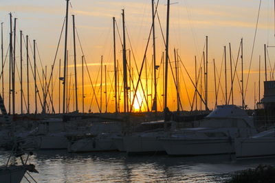 Sailboats moored on harbor against sky during sunset