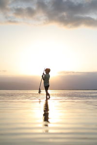 Full length of man standing in sea against sky during sunset