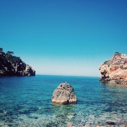 Rocks in sea against clear blue sky