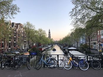 Bicycles parked by canal against sky in city