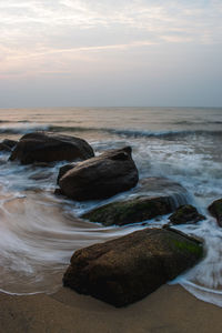 Rocks on beach against sky during sunset