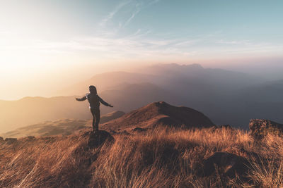 Man standing with arms outstretched on land during sunset