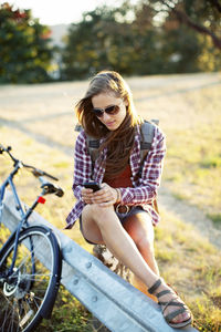 Young woman using mobile phone while sitting on tree stump