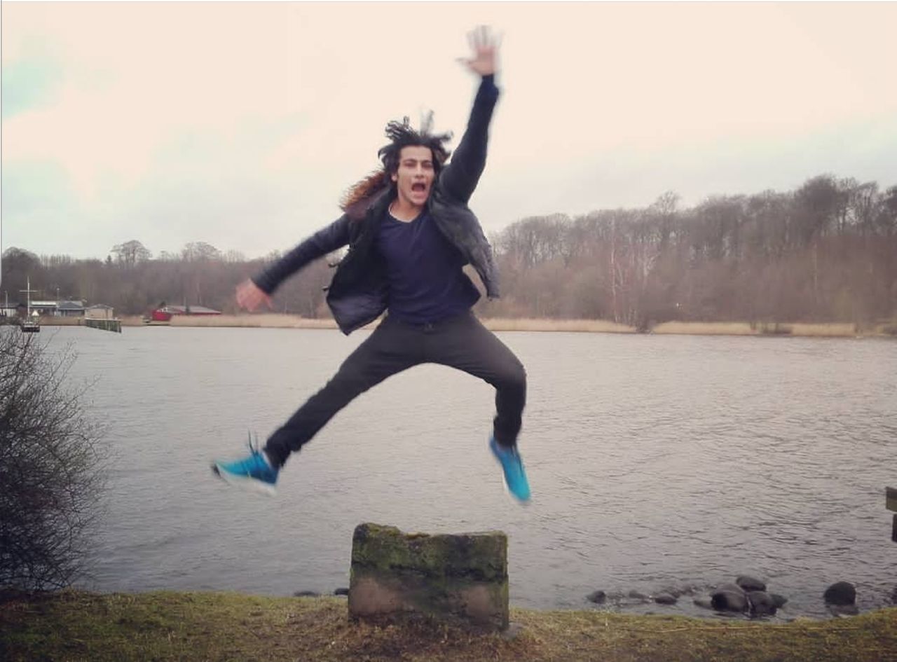 FULL LENGTH OF YOUNG WOMAN JUMPING AGAINST WATER