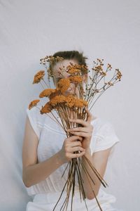 Low angle view of woman holding flowering plant against white wall