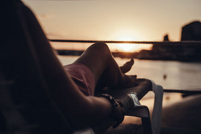 Low section of woman relaxing on lounge chair during sunset