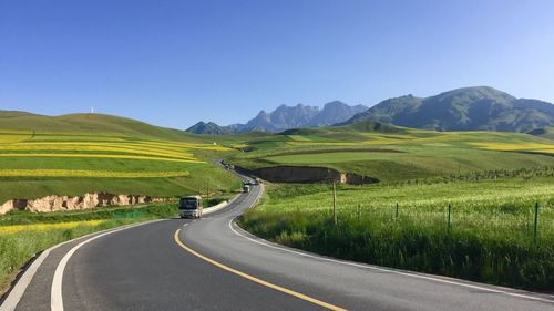 Road leading towards mountains against clear sky