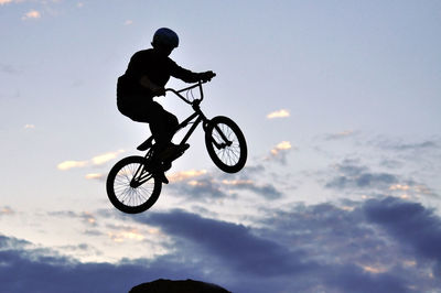 Low angle view of silhouette man riding bicycle against sky