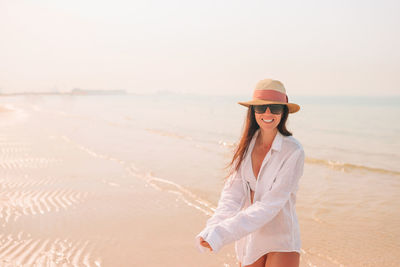 Portrait of smiling young woman standing on beach against sky