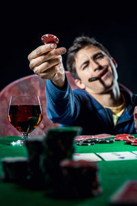 Man playing poker with whiskey and cigar against black background