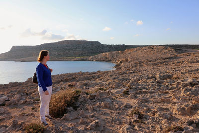 Full length of woman standing on rock formation by sea against sky